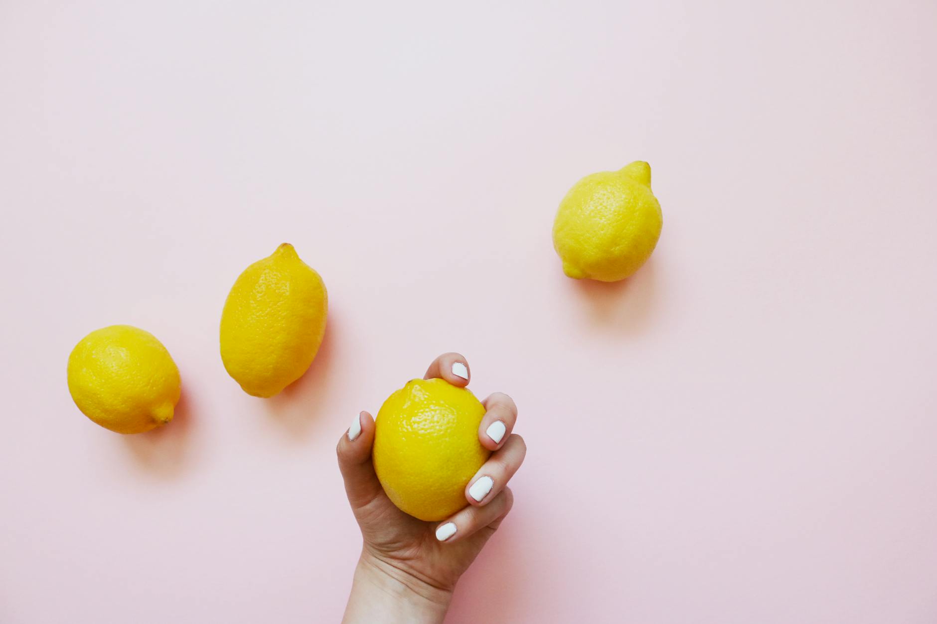 A hand holding fresh lemons on a soft pink background, symbolizing pleasure and vitality