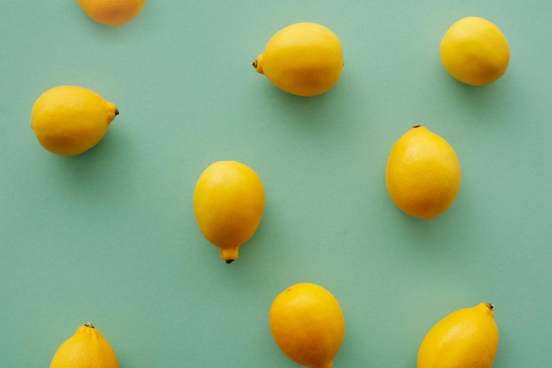 Fresh bright yellow lemons arranged on a pastel green background in a vibrant flat lay composition