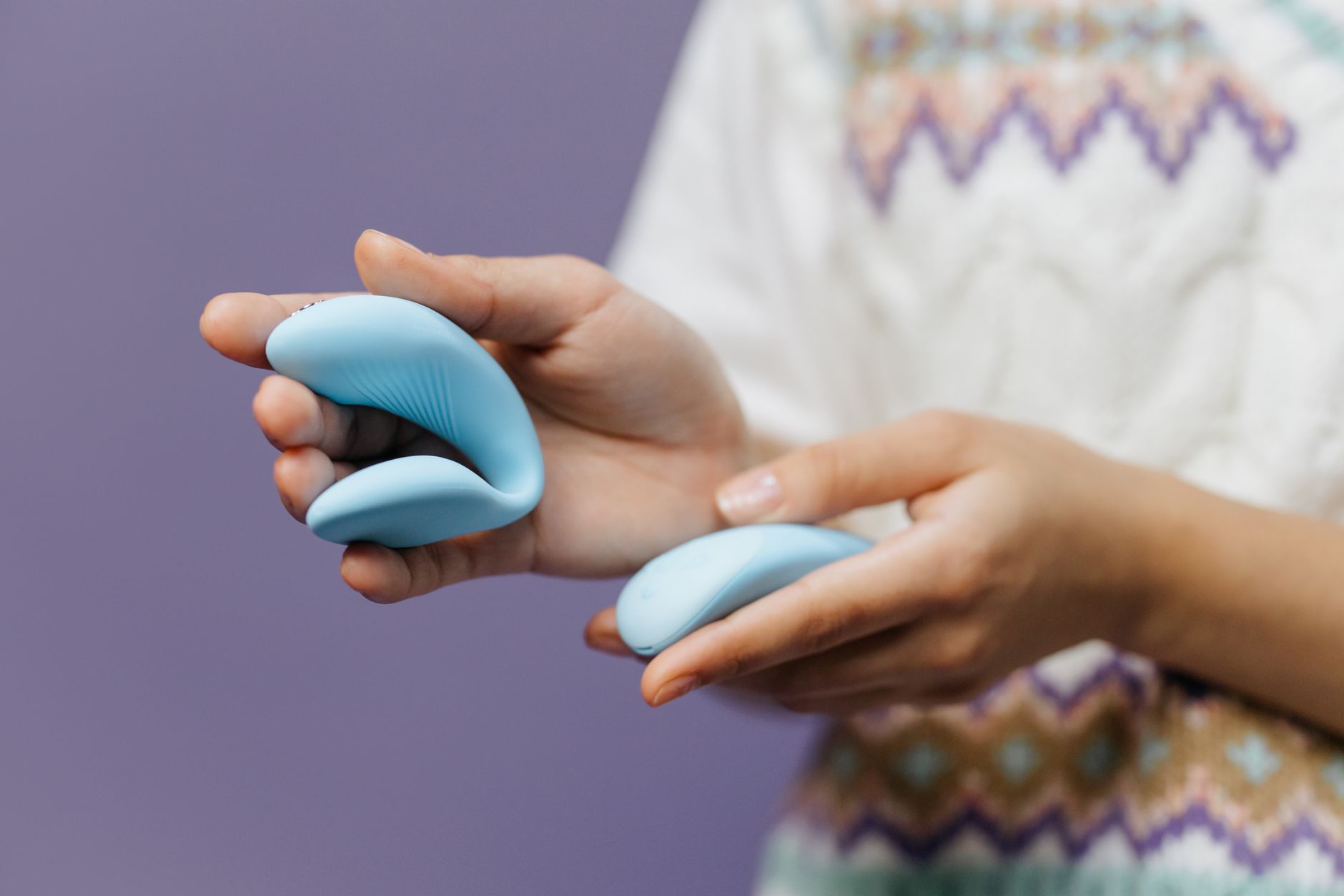 Close-up of hands holding a sleek blue suction vibrator against a purple background