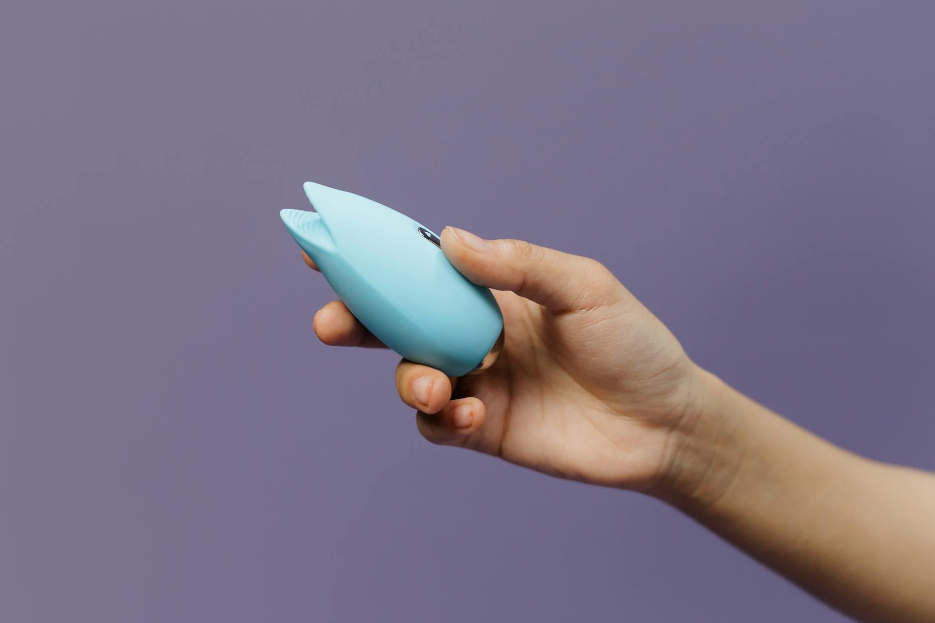 A hand holding a blue silicone clitoral vibrator against a purple background, representing reclaiming pleasure during medication