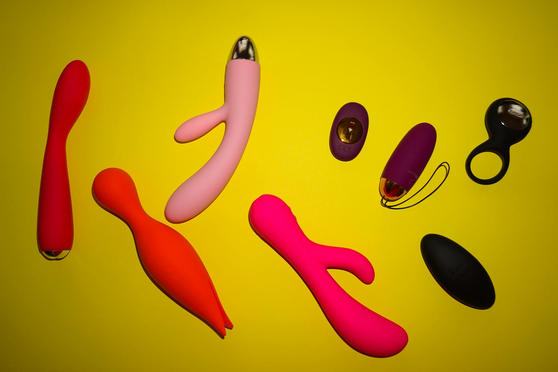 Two hands holding pink and blue vibrators together against a pastel background